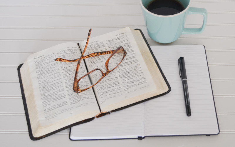 This is a picture of an open Bible with a pair of glasses, a journal and a cup of coffee.